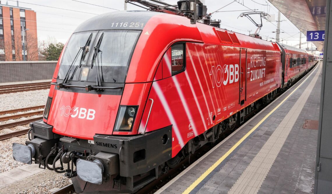 Öffentliches Verkehrsmittel (ÖBB-Zug) fährt in Bahnhof ein, damit Passagiere zusteigen können.