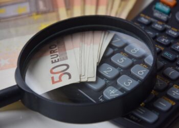 Ein Symbolbild zeigt Taschenrechner, Geldscheine und eine Lupe, um "Steuergeld" zu veranschaulichen.