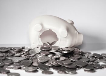 Symbolbild eines zur Seite gekippten Sparschweins, aus dem Münzen fallen.