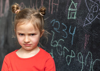 Unglückliches Mädchen vor beschriebener Tafel symbolisiert Frust über hohe Preise