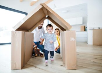 Symbolbild für Wohnbau-Krise und Traum vom Eigenheim in NÖ: Familie mit Kind vor gebasteltem Kartonhaus.