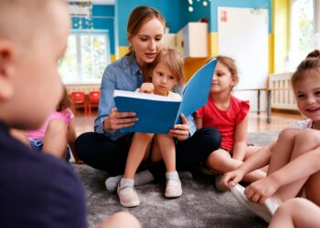 Symbolbild Kinderbetreuung: Ein Kind und eine Betreuungsperson lesen gemeinsam ein Buch in einer Lernumgebung.