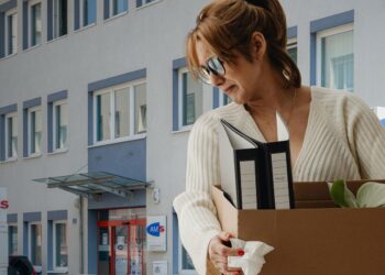 Montage aus zwei Fotos: Frau hält Kiste mit Pflanze (Karolina Grabowska, Unsplash) und Gebäude des AMS Oberwart (Thomas Ledl, Wikimedia Commons, CC BY-SA 4.0).