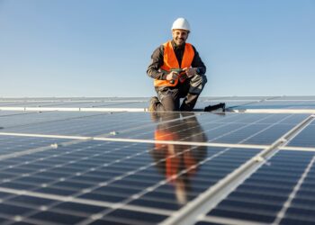 Symbolbild zeigt einen lächelnden Arbeiter, der an der Installation einer Photovoltaik-Anlage arbeitet.