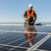 Symbolbild zeigt einen lächelnden Arbeiter, der an der Installation einer Photovoltaik-Anlage arbeitet.