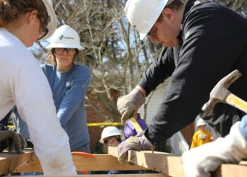 Das Symbolbild zeigt eine Gruppe arbeitender Menschen bei der Holzbearbeitung im Freien.