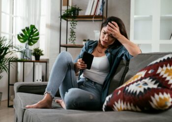 Junge Frau blick sorgenvoll auf Mobiltelefon