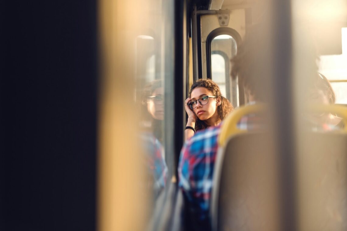 Junge Frau, die betrübt aus dem Fenster eines öffentlichen Verkehrsmittels schaut.