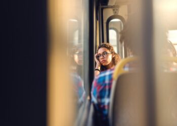 Junge Frau, die betrübt aus dem Fenster eines öffentlichen Verkehrsmittels schaut.