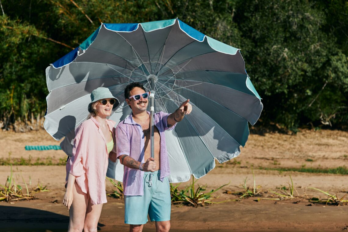 Abtenteuerlustige, junge Menschen, die Schutz unter einem Sonnenschirm suchen